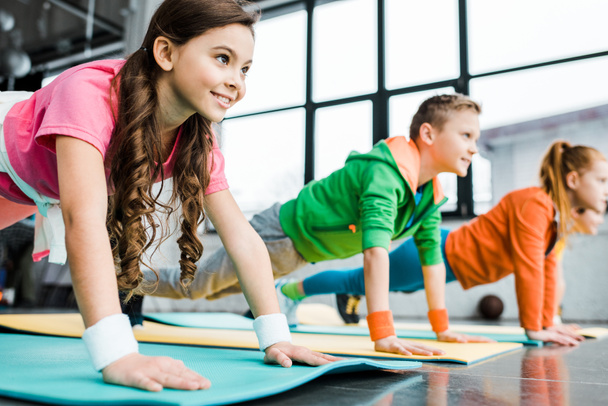 Niños sonrientes haciendo ejercicio de tablón en colchonetas de fitness
 - Foto, imagen