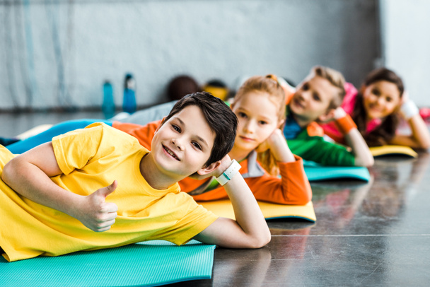 Fröhliche Kinder liegen in Turnhalle auf Fitnessmatten - Foto, Bild
