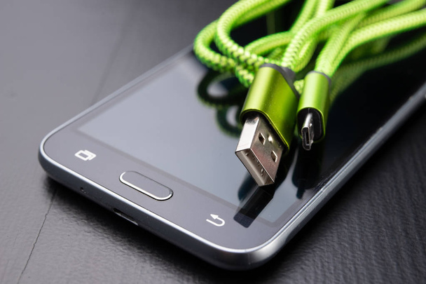A usb cable for data transfer and phone charging. Telephone and accessories on the table. Dark background. - Zdjęcie, obraz