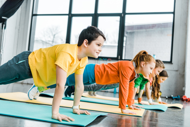 Niños preadolescentes haciendo ejercicio de tablón juntos en el gimnasio
 - Foto, imagen