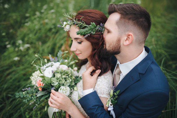 Groom tenderly embracing bride standing behind. Bride with wreath of real flowers. - Fotografie, Obrázek