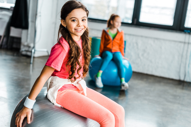 Long-haired kid in pink sportswear sitting on fitness ball - Photo, Image