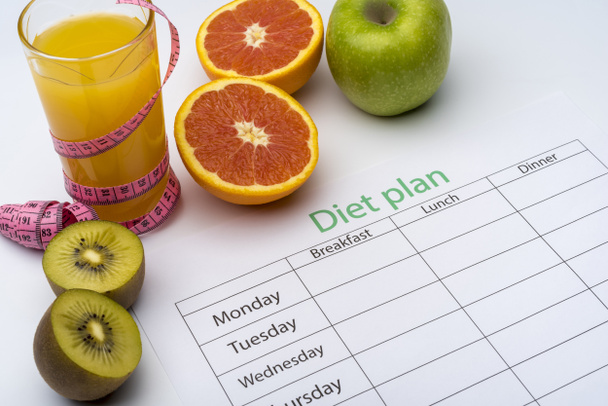 オレンジ ジュースのグラスの横にある紙切れにダイエット計画。フレッシュなグレープ フルーツ、キウイ、白い背景上のリンゴ。健康的な食事の概念. - 写真・画像