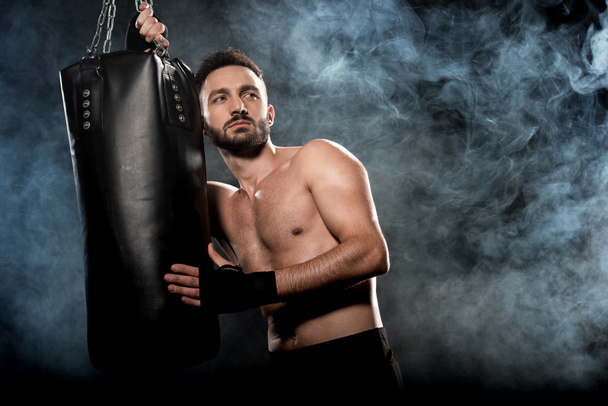 boxeador atlético pensativo que sostiene el saco de boxeo en negro con humo
 - Foto, Imagen