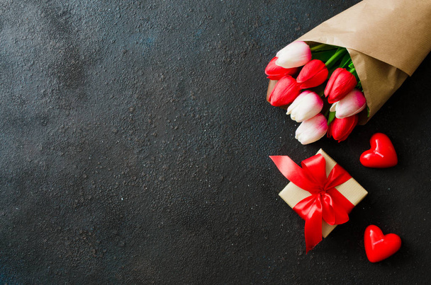 Rekreační zázemí jarními květy. Kytice z tulipánů, dárkové krabičky a dekorativní srdce na tmavém pozadí. Přání na Valentýna, ženy nebo matky den. Plochá ležel, horní pohled, kopie prostor - Fotografie, Obrázek