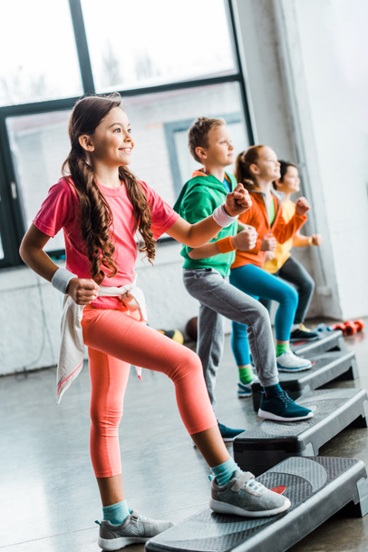 Crianças sorridentes treinando em ginásio com plataformas passo
 - Foto, Imagem