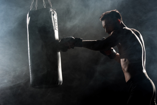 silhouette d'athlète en gants de boxe frappant le sac de boxe sur noir avec de la fumée
 - Photo, image