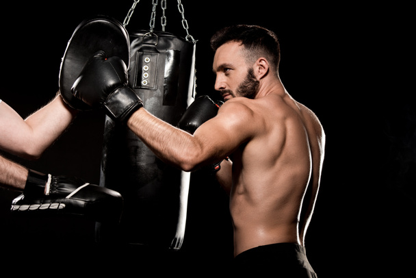 handsome sportsman fighting with man in punching gloves isolated on black - Photo, Image