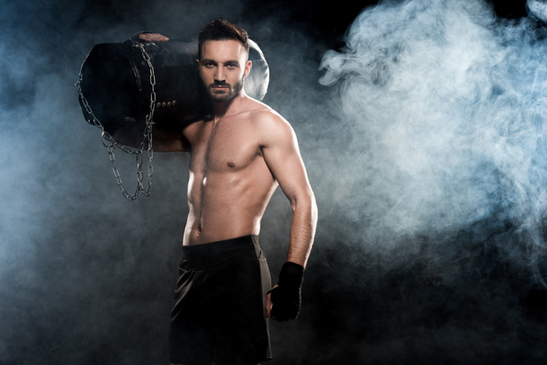 boxeador muscular que sostiene el saco de boxeo en el hombro negro con humo
 - Foto, imagen