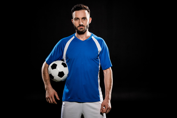 bearded football player standing with ball isolated on black - Foto, imagen