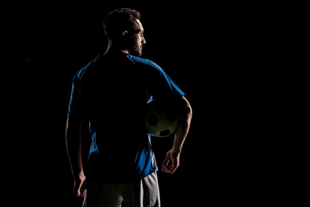 σιλουέτα του μυϊκή αθλητή κρατώντας την μπάλα που απομονώνονται σε μαύρο - Φωτογραφία, εικόνα