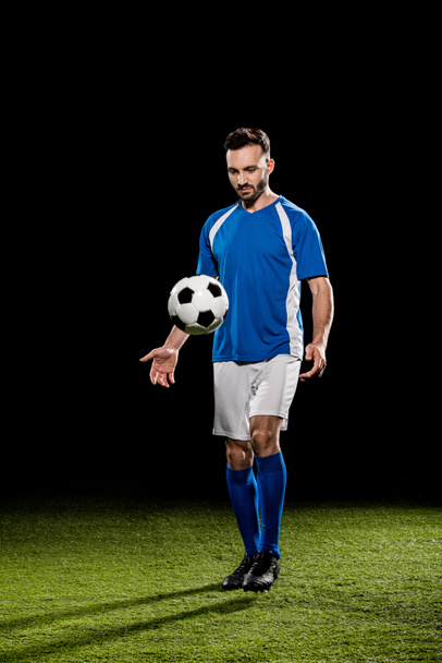 bearded sportsman in uniform training with ball on grass isolated on black - Фото, изображение