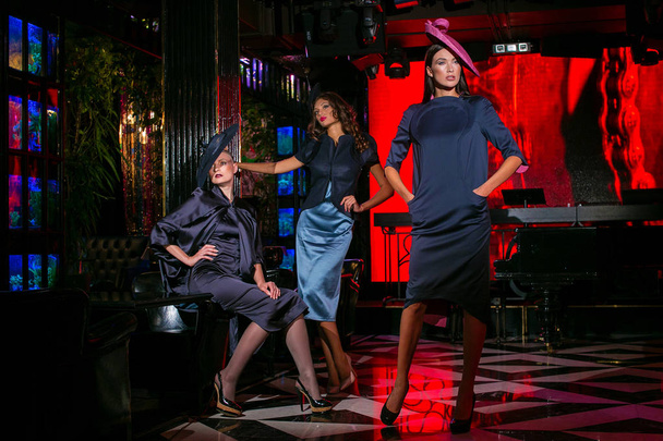 Three beautiful models in a stylish designer clothes posing in a nightclub - Foto, Imagen