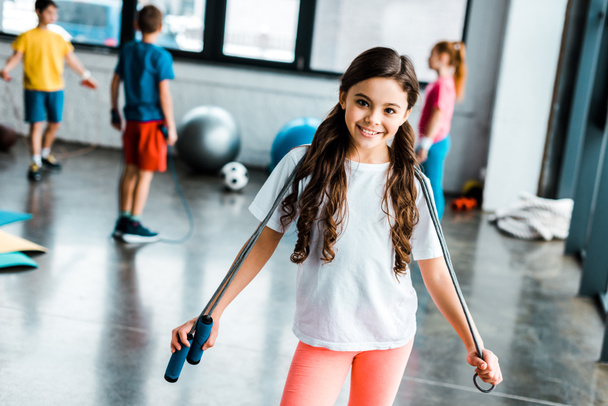 Cute brunette kid holding jump rope and smiling at camera - Foto, Imagen