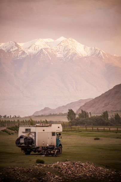 Een camper en een zijspan motorfiets gesteund door een besneeuwde bergketen. - Foto, afbeelding