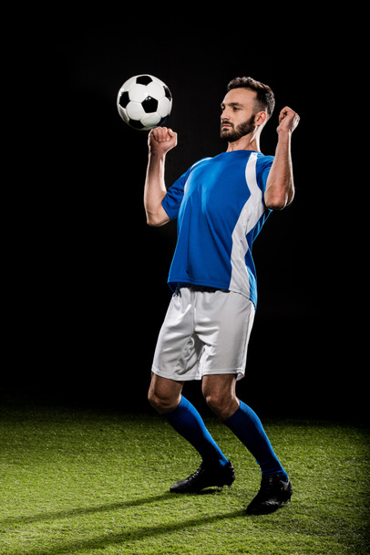 athletic football player in uniform jumping with ball isolated on black - Foto, Imagem