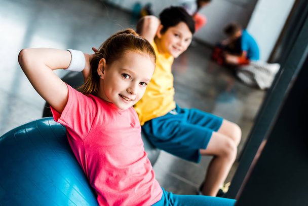 Crianças sorridentes fazendo exercícios abdominais com bolas de fitness no ginásio
 - Foto, Imagem