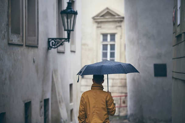Uomo con l'ombrello che cammina sotto la pioggia. Old city street in Prague, Repubblica Ceca
  - Foto, immagini