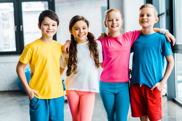 Niños preadolescentes alegres sonriendo y abrazándose en el gimnasio
 - Foto, Imagen