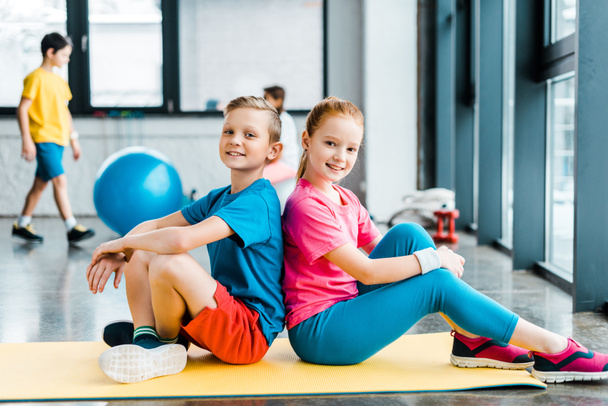 Adorable kids sitting back to back on fitness mat - 写真・画像