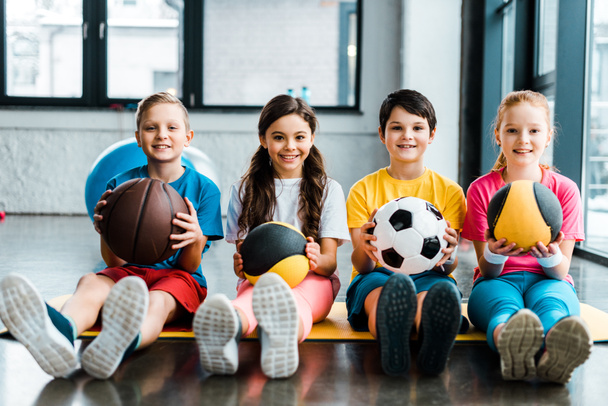 Preteen kids sitting on fitness mat with balls - Photo, image