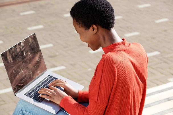 Retrato lateral de mujer joven sentada afuera con computadora portátil
 - Foto, imagen