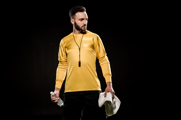 handsome referee holding bottle and towel in hands isolated on black - Φωτογραφία, εικόνα