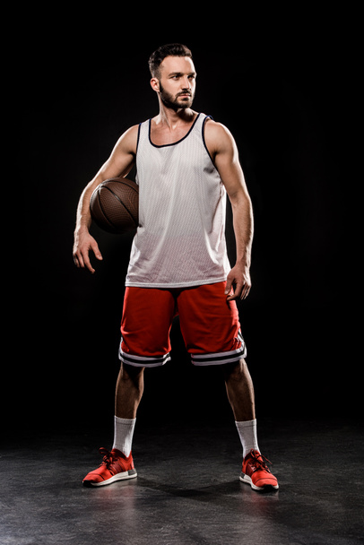 muscular basketball player standing with ball on black background - Φωτογραφία, εικόνα
