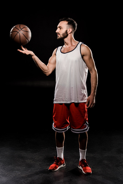 bebaarde basketbal speler draaiende bal op vinger op zwarte achtergrond - Foto, afbeelding