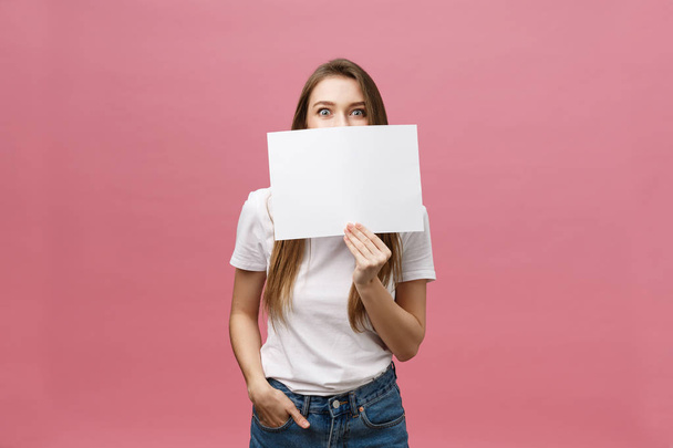 Junge kaukasische Frau mit leerem Papierbogen vor isoliertem Hintergrund erschrocken mit einem Überraschungsgesicht, ängstlich und aufgeregt mit ängstlichem Ausdruck - Foto, Bild