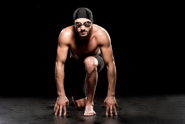 athletic swimmer standing in start position on black background  - Foto, immagini