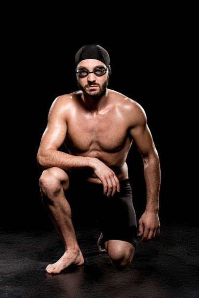 guapo nadador sentado en gorra de natación y gafas sobre fondo negro
 - Foto, Imagen