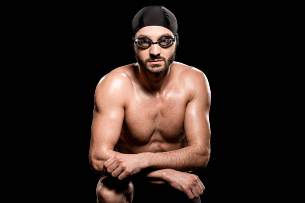 handsome swimmer sitting in swimming cap and goggles isolated on black - 写真・画像