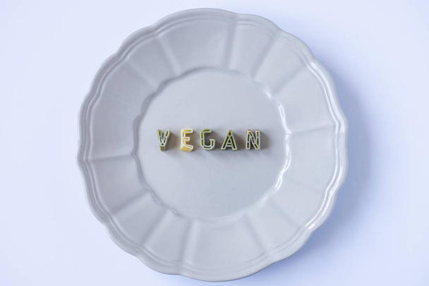 The word "vegan" written with green pasta letters in a beige dish. Veganism background, conceptual wallpaper. Top view. - Photo, Image