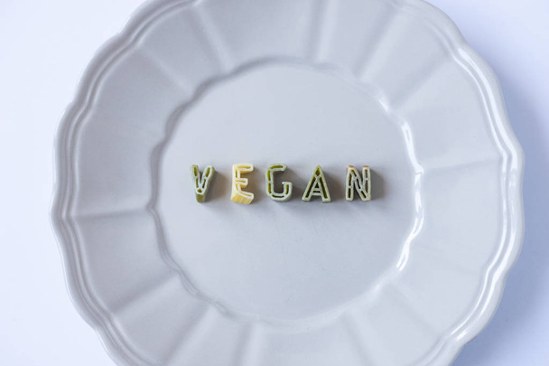 das Wort "vegan" mit grünen Nudelbuchstaben in einem beigen Gericht geschrieben. Veganismus Hintergrund, konzeptionelle Tapete. Nahaufnahme von oben. - Foto, Bild