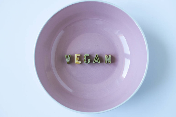 La palabra "vegano" escrita con letras de pasta verde en un plato beige. Fondo vegetariano, fondo de pantalla conceptual
. - Foto, Imagen
