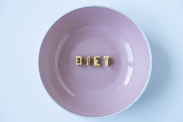 La palabra "dieta" escrita con letras de pasta real en un plato rosado. Fondo de pantalla conceptual, vista superior
. - Foto, Imagen