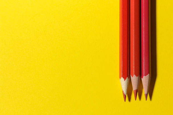 Three red pencils on a bright yellow background. Place for text. view from above - Foto, Imagem