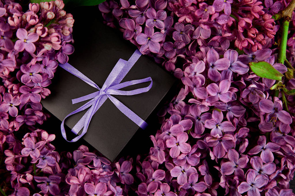 Чорні маленькі подарункові коробки, обгорнуті фіолетовою, фіолетовою стрічкою, прикрашені квітковим натуральним бузком. Квіткові елементи декору. Копіювати простір. Місце для тексту
.  - Фото, зображення