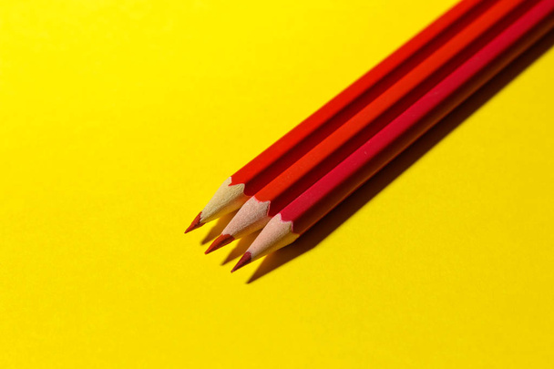 Three red pencils on a bright yellow background with a hard shadow. stationery - Zdjęcie, obraz