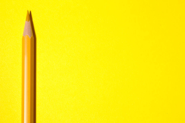 een geel potlood op een helder gele achtergrond met een harde schaduw. briefpapier. bovenaanzicht. ruimte voor tekst - Foto, afbeelding