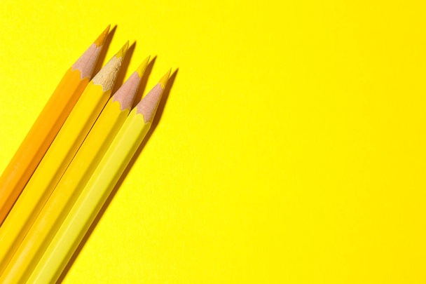 Three yellow pencils on a bright yellow background with a hard shadow. stationery. top view. space for text - 写真・画像