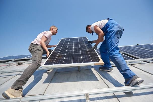 Eletricistas levantando módulo solar azul no telhado da casa moderna
 - Foto, Imagem
