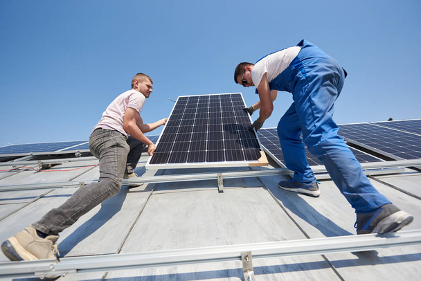Electricians lifting blue solar module on roof of modern house - Photo, Image