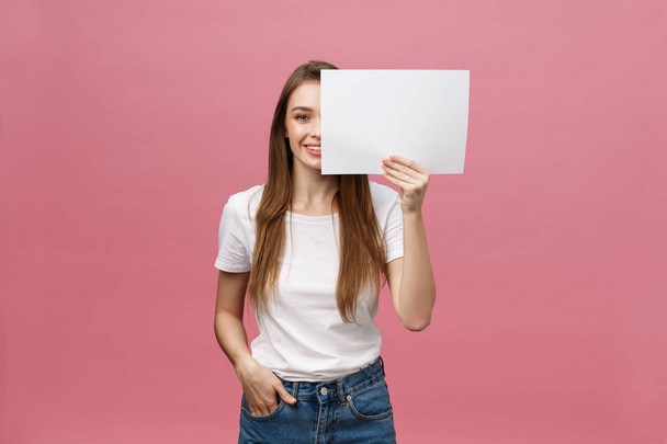 Close up portrait of positive laughing woman smiling and holding white big mockup poster isolated on pink background - Fotografie, Obrázek