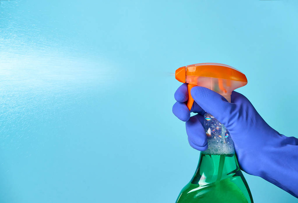 Una mano en un guante azul sostiene un aerosol de limpieza. Fondo azul conceptual
. - Foto, imagen