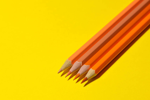Lápices naranjas sobre un fondo amarillo brillante con una dura sombra. espacio para texto
 - Foto, imagen