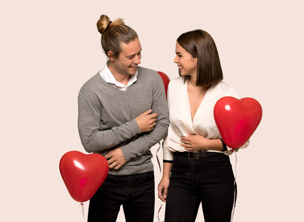 Couple in valentine day smiling a lot while putting hands on chest over isolated background - Zdjęcie, obraz