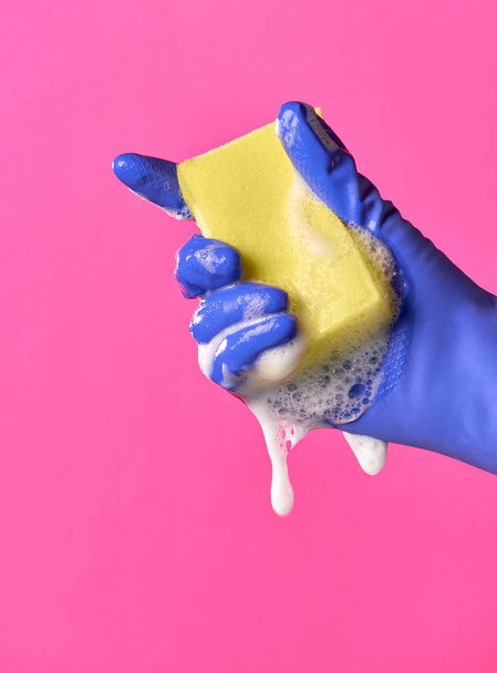 手袋をはめた手の衛生の黄色いスポンジを圧縮します。水、泡。ピンクの背景. - 写真・画像