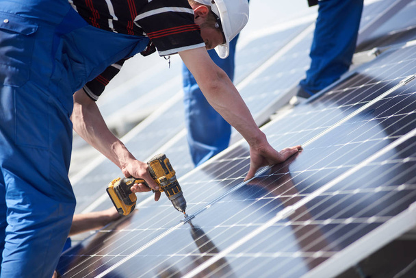 Elektriker montieren blaues Solarmodul auf dem Dach eines modernen Hauses. Ökologisches Konzept für alternative erneuerbare Energien. - Foto, Bild
